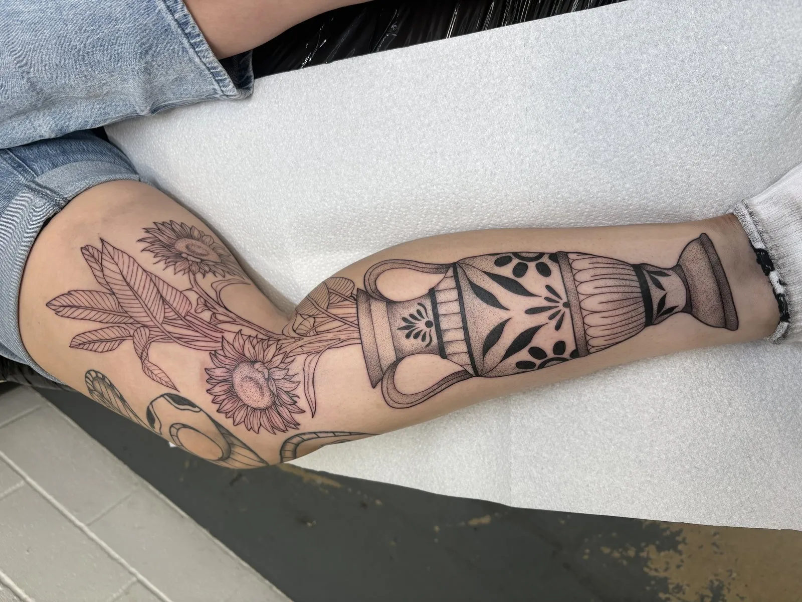 Sunflowers in a Greek urn, blackwork and stipple shaded leg tattoo by Lana at Shade Studio Peterborough